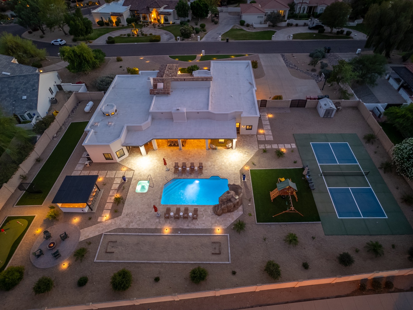 Aerial view of a luxury vacation estate featuring a sparkling pool, private tennis court, outdoor entertaining areas, and manicured grounds in an upscale neighborhood.