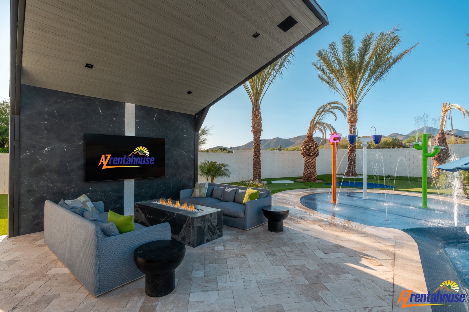 Covered outdoor lounge with modern fireplace seating and kids' splash area surrounded by desert palms.
