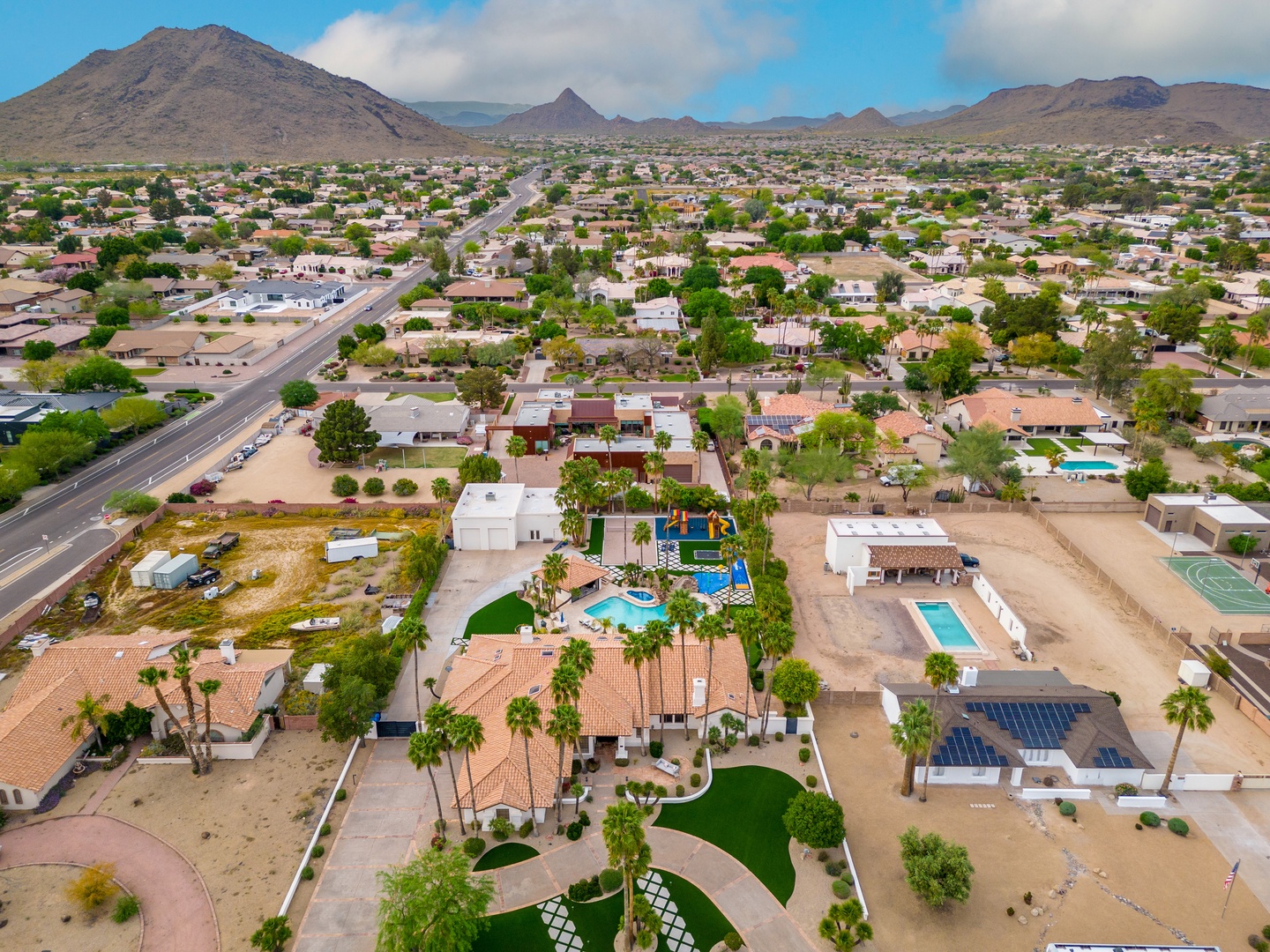 Aerial view showcasing the property nestled in a residential neighborhood, with dramatic desert mountain ranges framing the horizon under a clear Arizona sky.