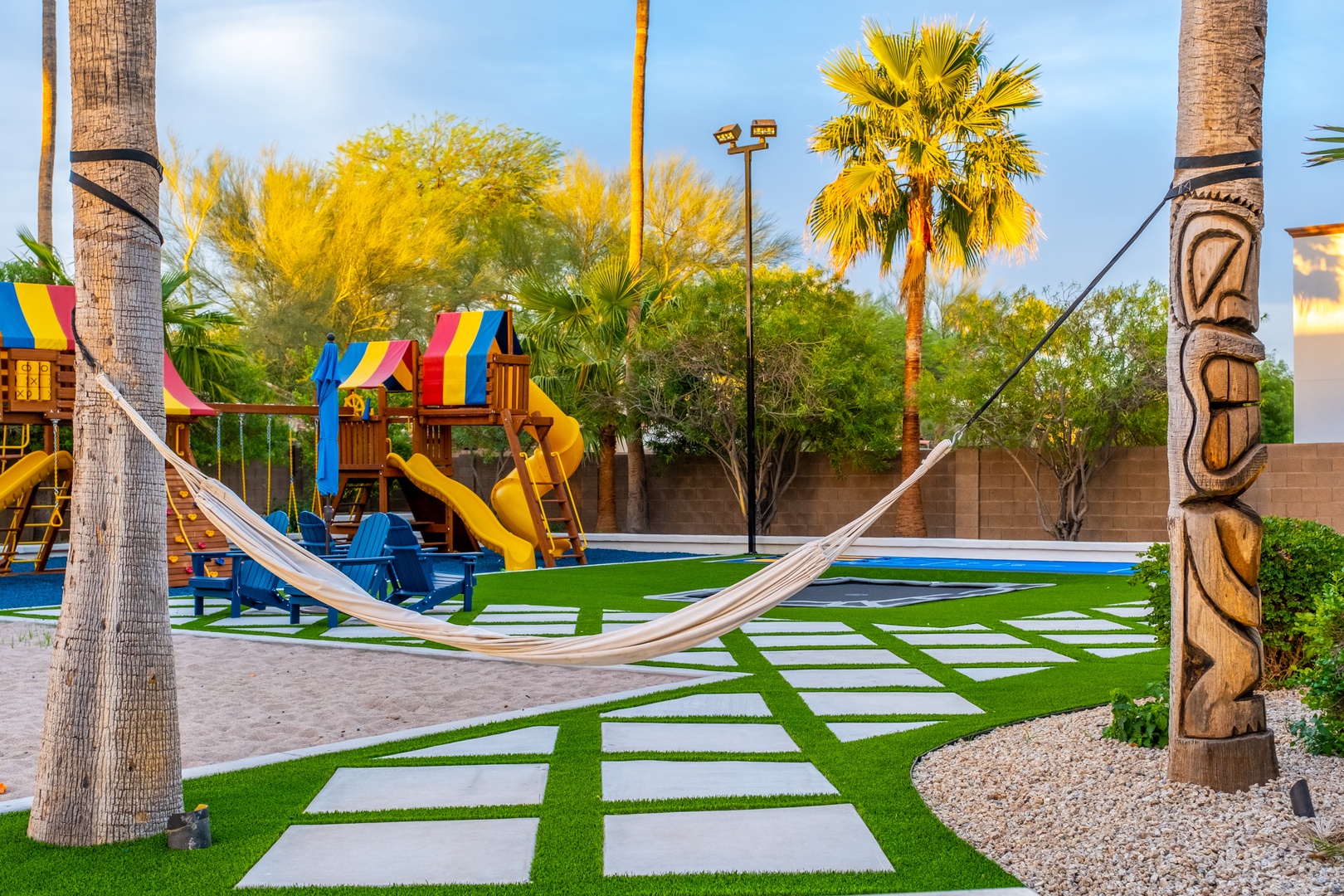 A vibrant backyard oasis features a colorful playground, relaxing hammock strung between palm trees, sparkling pool, and spacious lawn with decorative stepping stones—perfect for families seeking fun and relaxation.