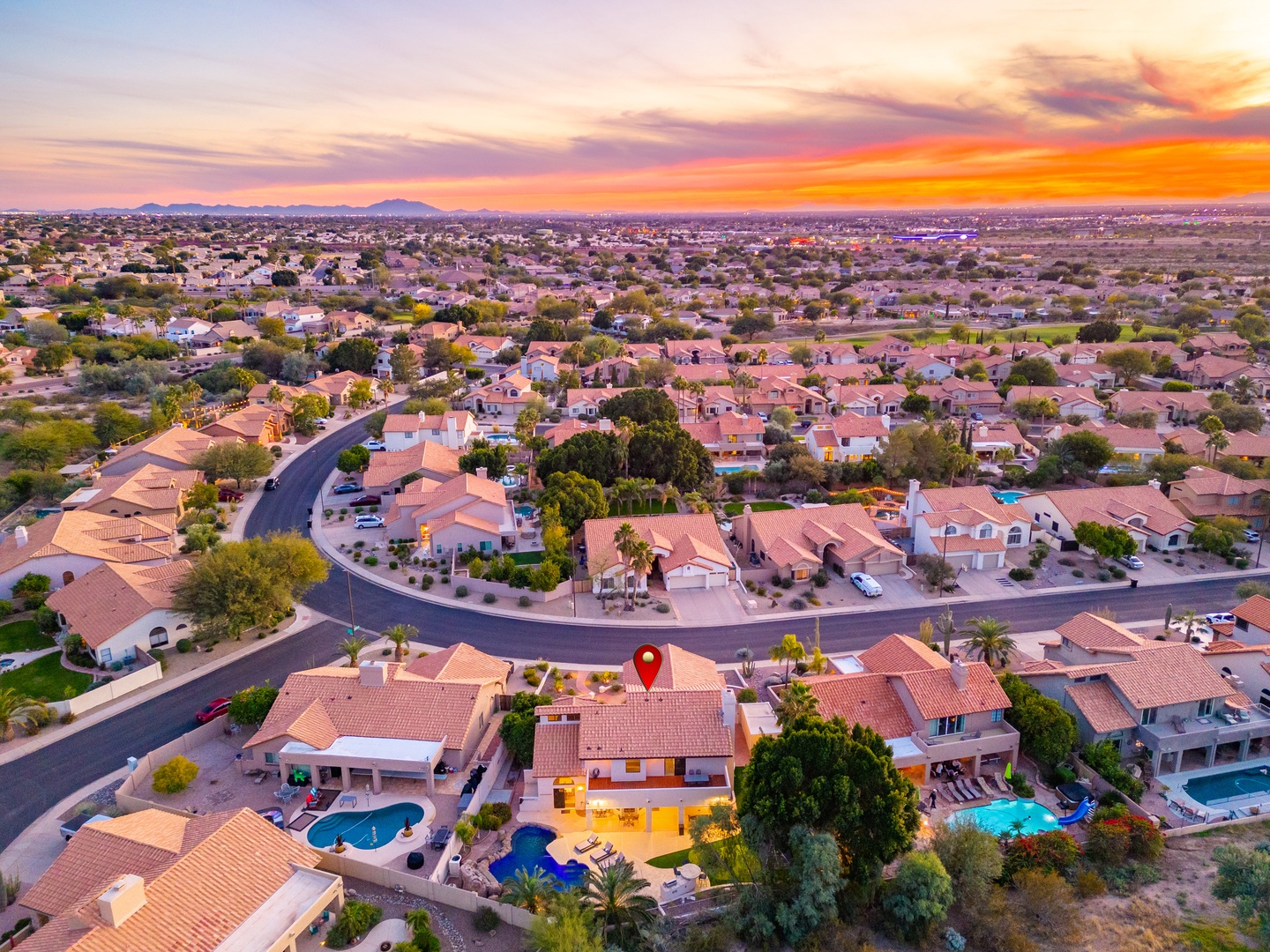 Aerial view of the property nestled in a serene residential neighborhood, captured during a stunning desert sunset with mountains on the horizon.