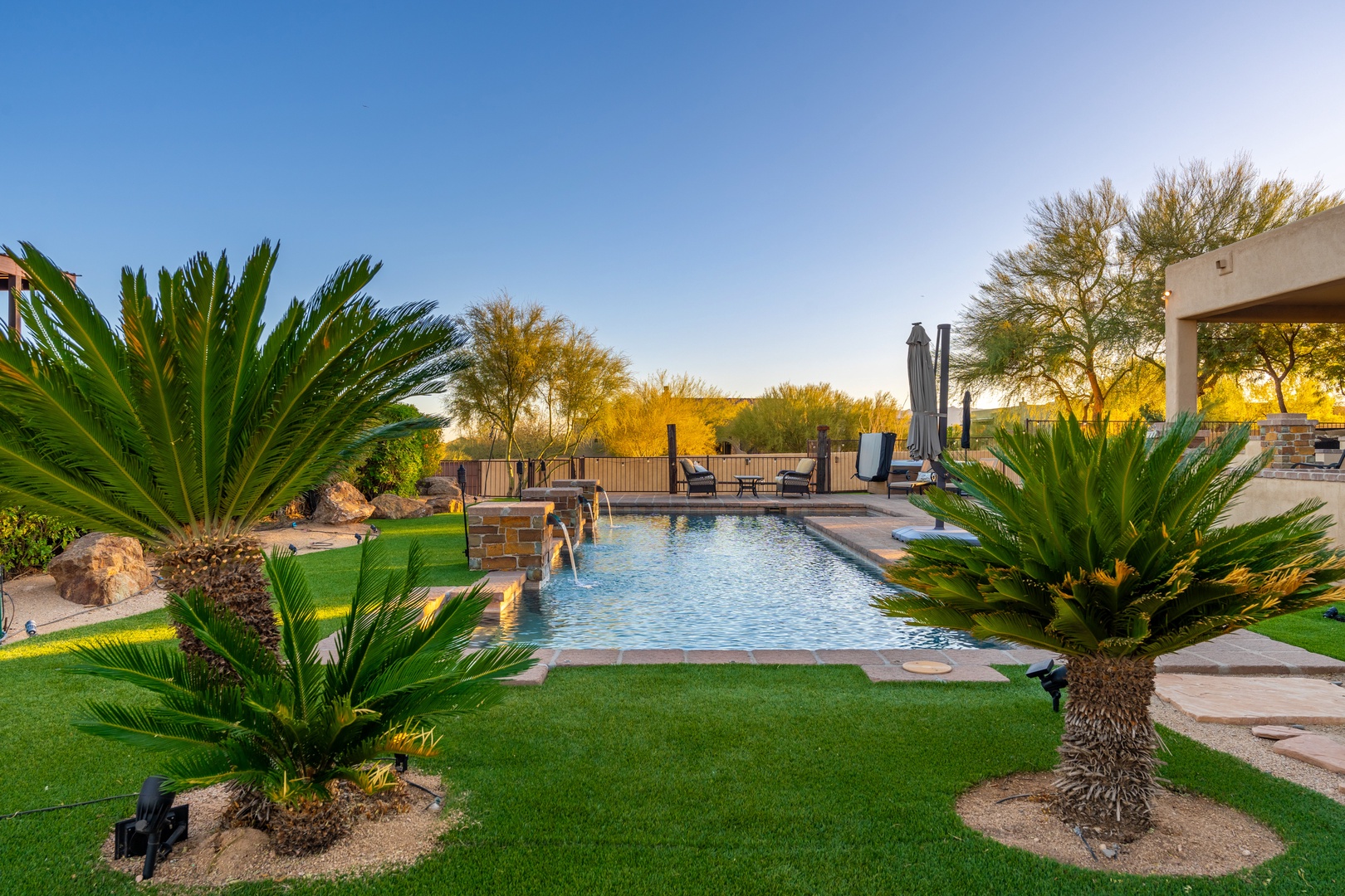 Expansive backyard oasis features a pristine pool surrounded by lush desert landscaping, palm trees, and mountain views—perfect for soaking in Arizona's golden sunsets.