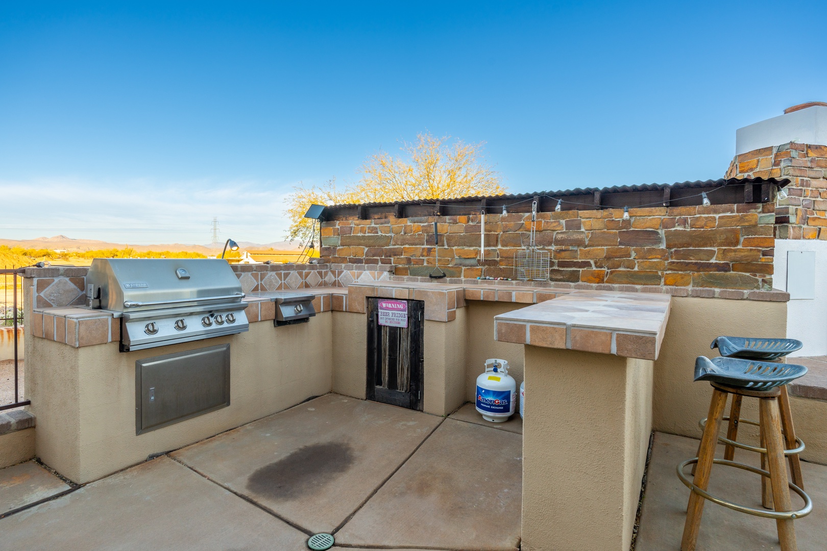 Outdoor kitchen with built-in grill and wine fridge, offering beautiful desert and mountain views as you prepare meals under clear blue skies.
