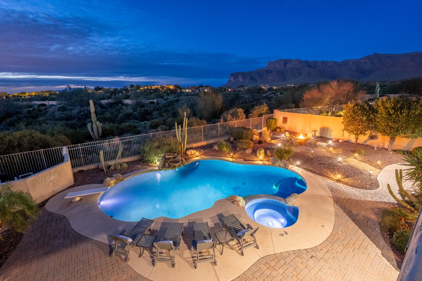 Twilight reveals a glowing pool and spa overlooking dramatic mountain vistas and desert landscapes, with illuminated pathways guiding your evening swim under the deepening sky.