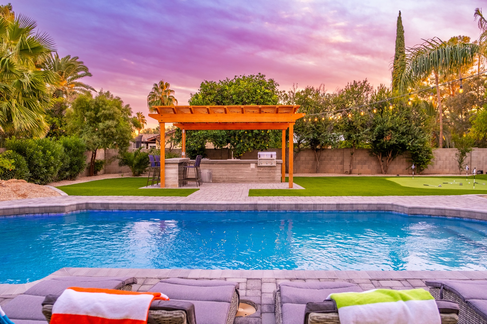 Stunning twilight backdrop frames a pristine pool and covered outdoor kitchen, perfect for entertaining under painted desert skies.