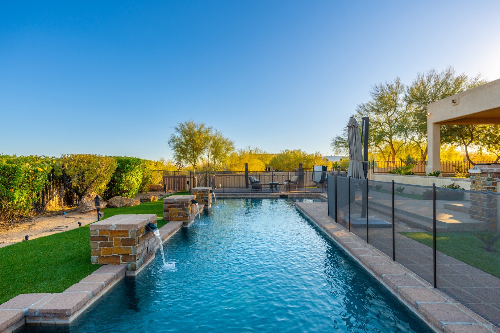 Sparkling pool with water features and spacious patio, framed by lush desert landscaping and golden-hour light—perfect for refreshing dips and sunset relaxation.