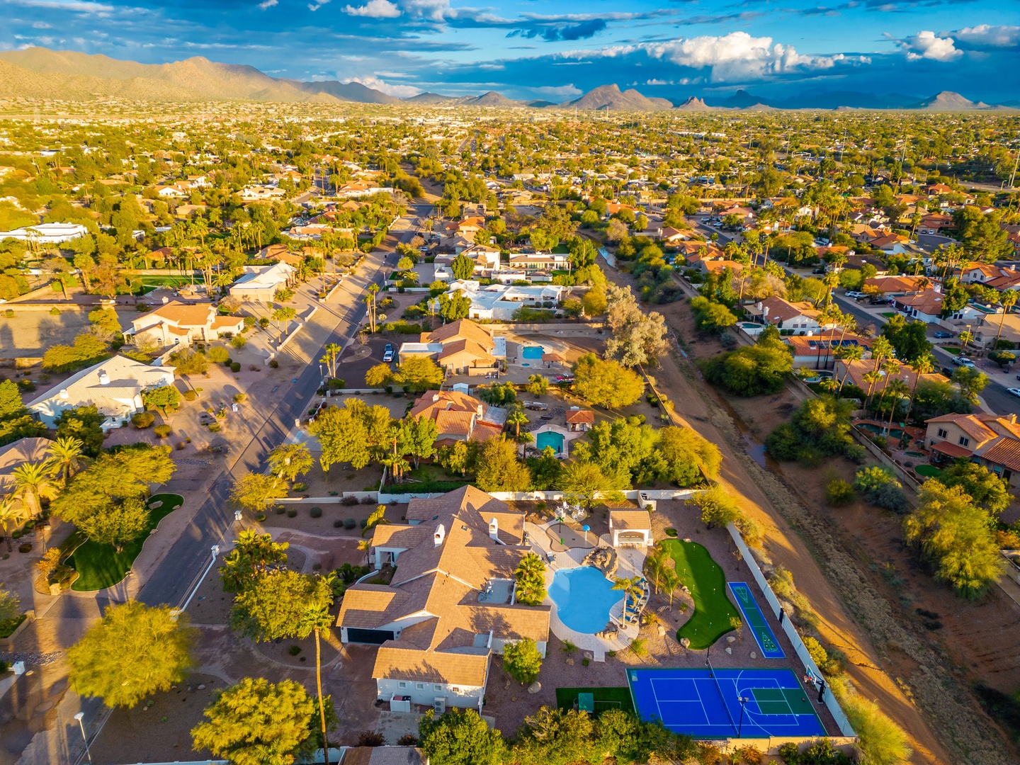 Aerial view of a spacious vacation rental property nestled in a scenic desert neighborhood, featuring private pools, tennis courts, and mountain vistas.