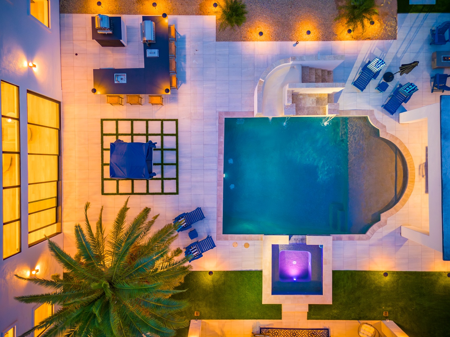 An aerial view showcasing the property's inviting layout with a central swimming pool, illuminated outdoor spaces, and tropical landscaping visible at dusk.