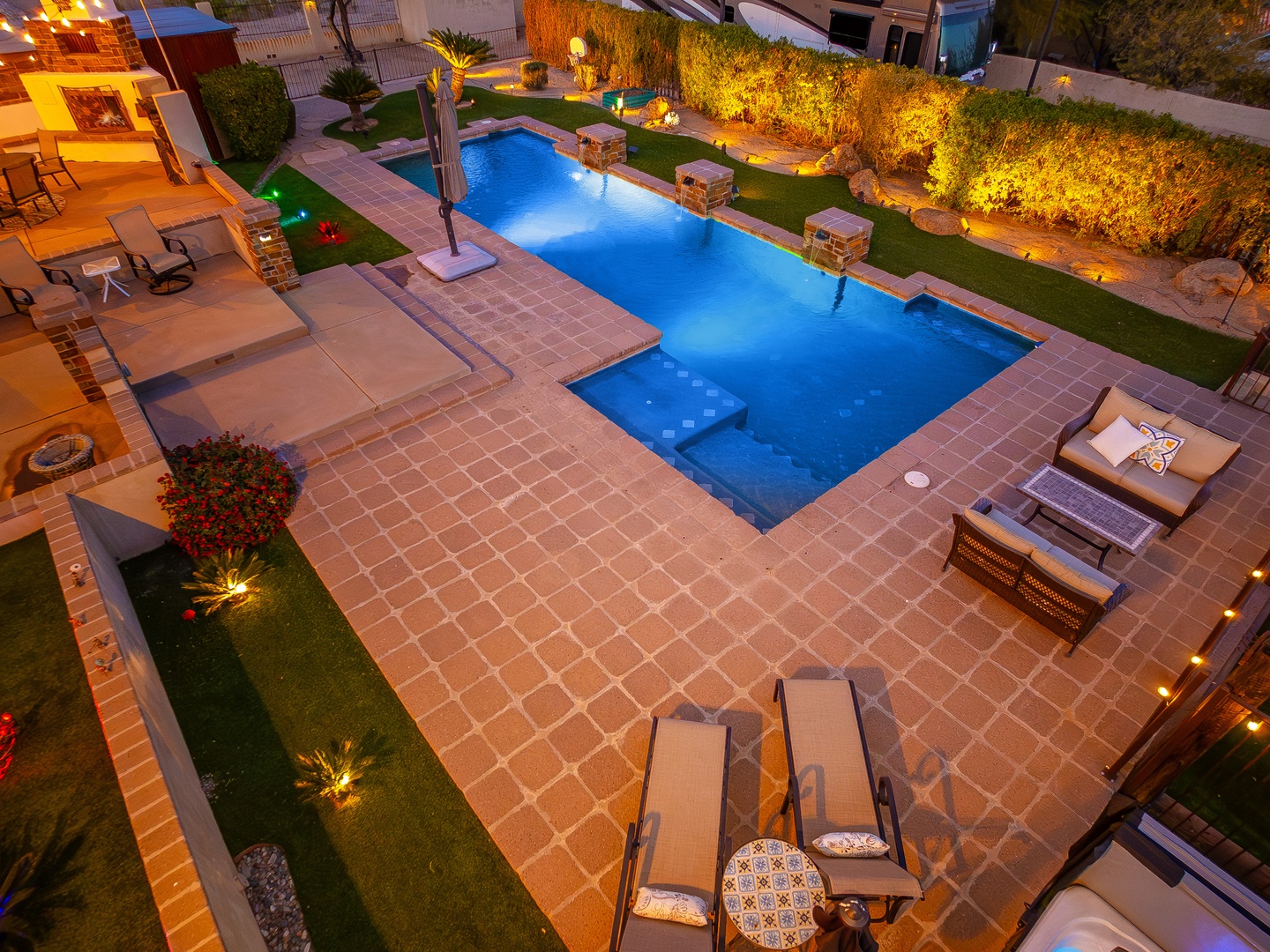 Aerial view of the beautifully lit pool and patio area at dusk, showcasing inviting lounge spaces and lush landscaping around the property.