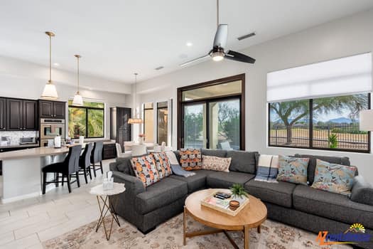 Unwind in your spacious open-concept living area featuring a plush sectional sofa and modern ceiling fan, perfect for relaxing after desert adventures.
