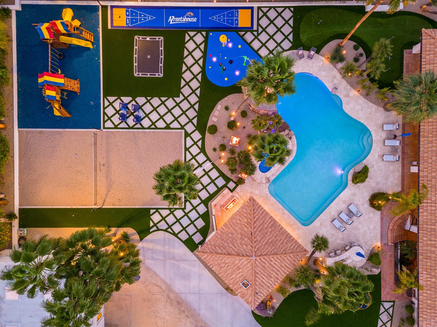 Aerial view of the resort showcasing a vibrant aqua park with colorful water slides, a free-form swimming pool with ambient lighting, sports courts, and lush palm-studded grounds.