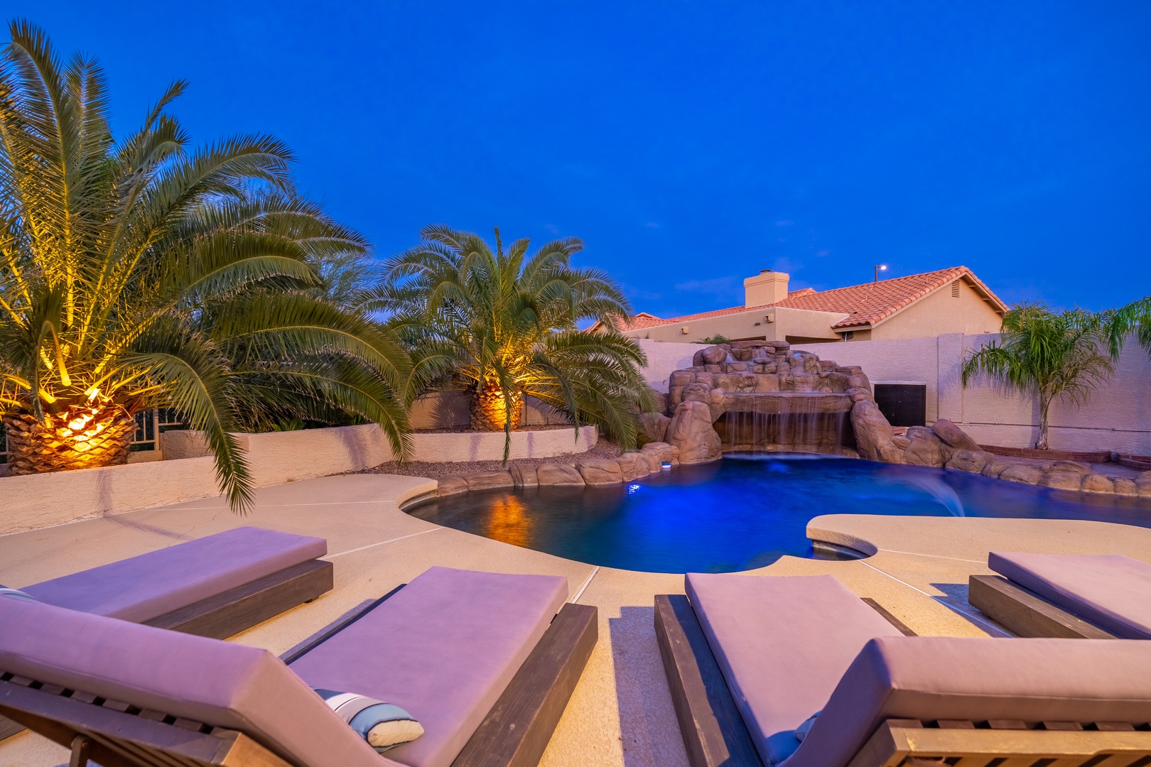 Your private resort awaits: soak in the glowing pool, unwind by the waterfall, or stargaze from luxurious loungers under swaying palms. Pure desert paradise at dusk.