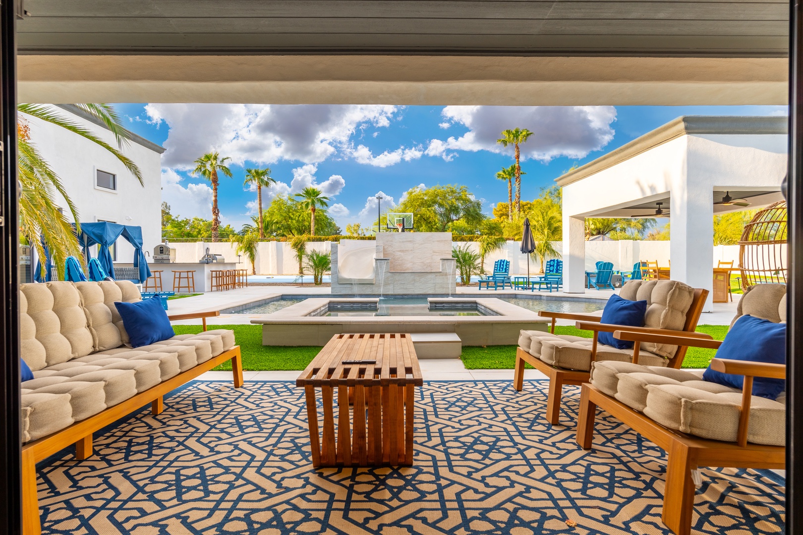 Relax in your private outdoor oasis with plush seating, sparkling pool, and lush palm trees creating a perfect desert escape under sunny skies.