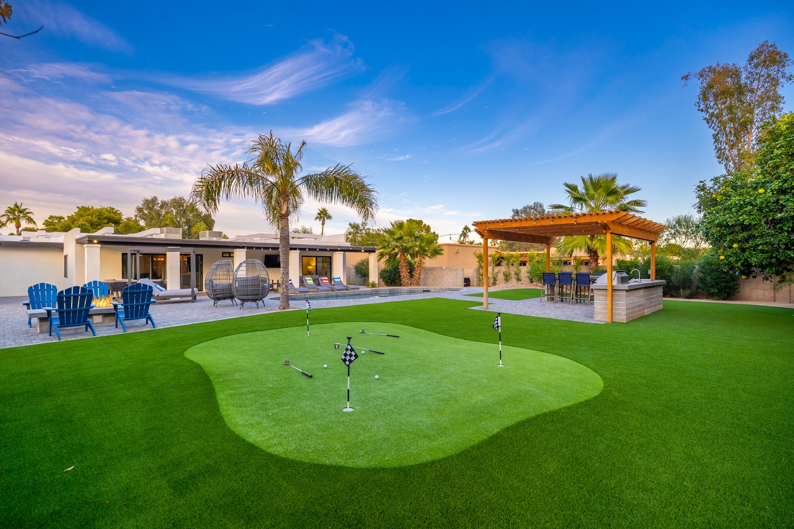 A private putting green stretches across the backyard beneath swaying palms, with cozy seating areas and a pergola-shaded patio perfect for evening gatherings under open skies.