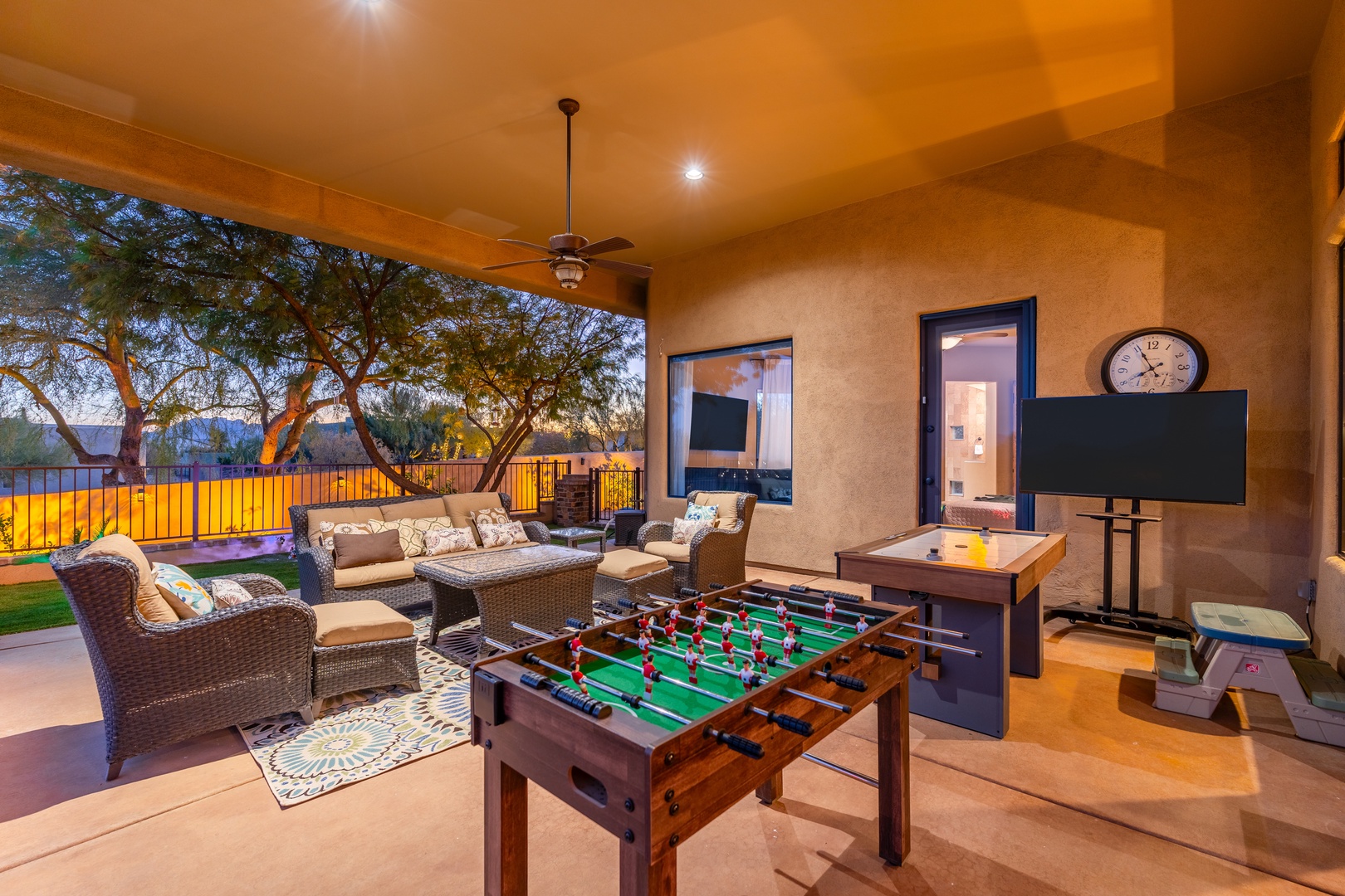 This expansive covered patio invites you to unwind with comfortable lounge seating, foosball for friendly competition, a mounted TV, and views of lush landscaping and the open yard beyond.