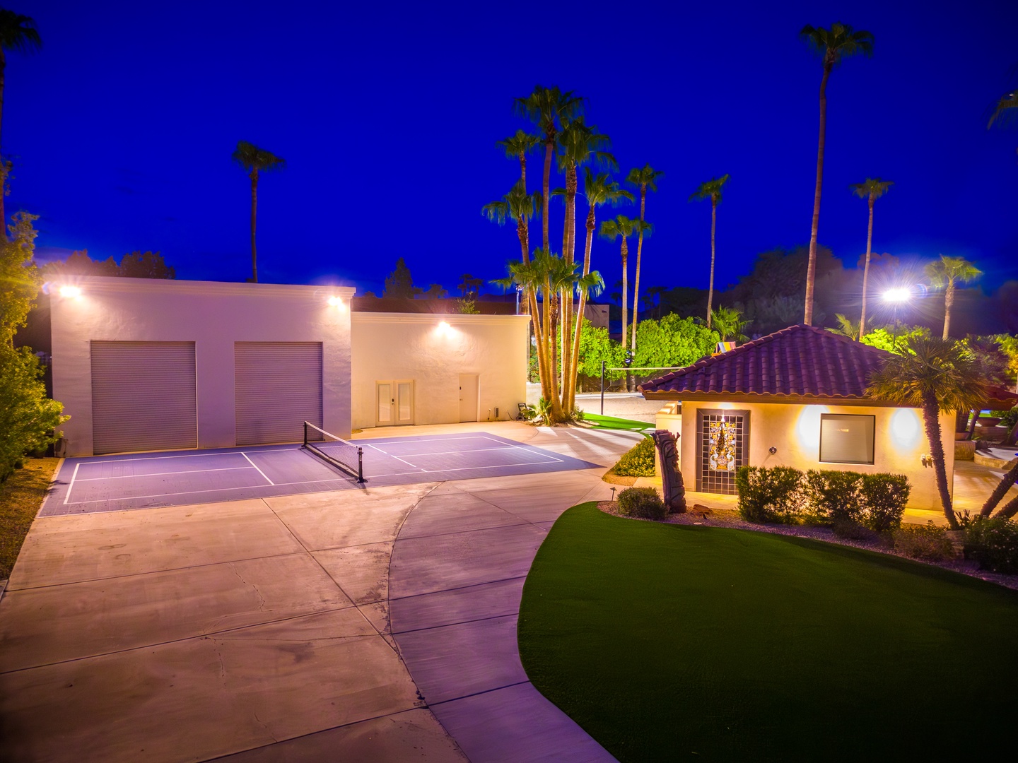 Twilight reveals a stunning desert oasis property featuring manicured lawns, towering palms, and dramatic blue-hour lighting illuminating the grounds and architecture.