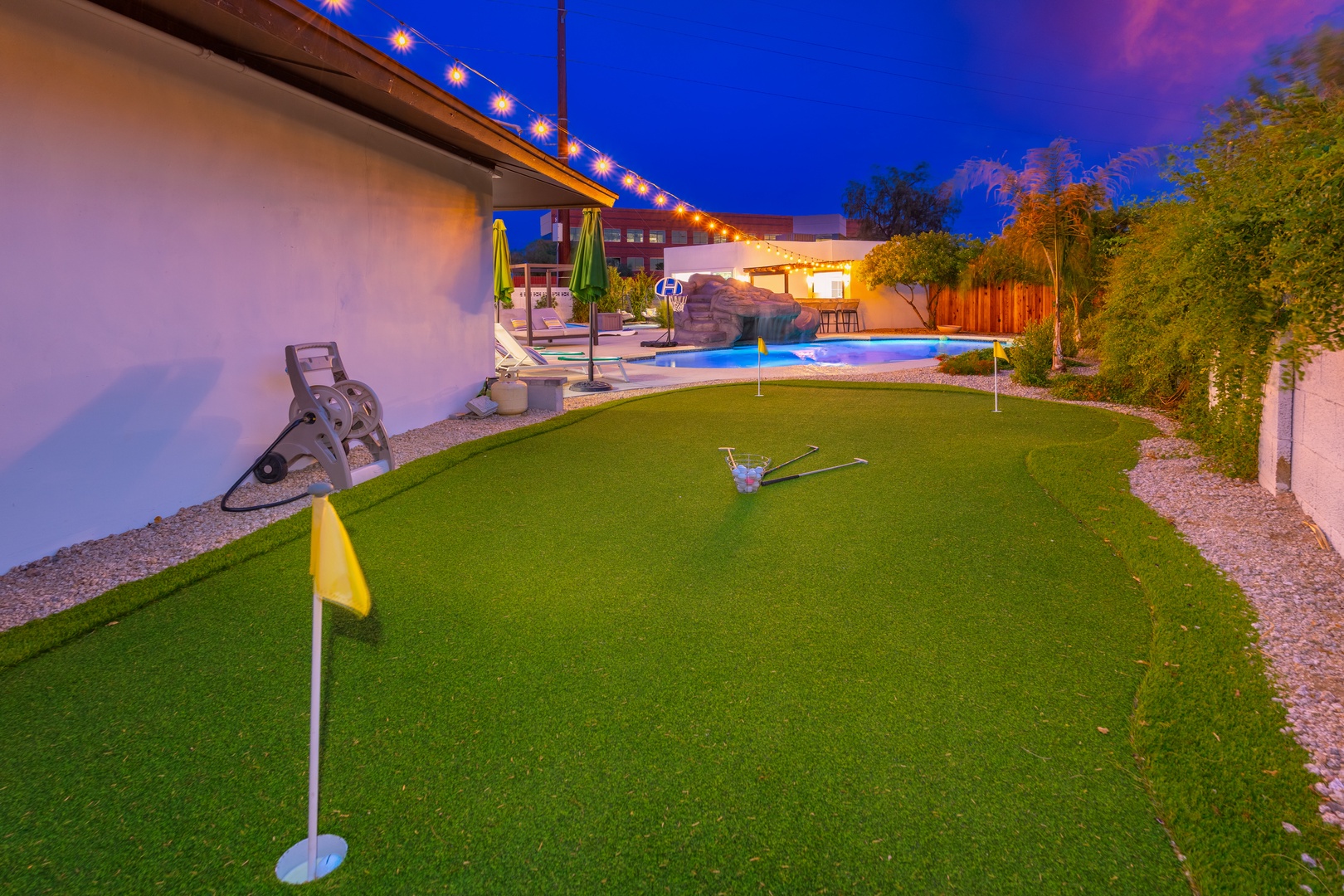 The private putting green invites friendly competition beneath string lights, while the sparkling pool and lush landscaping create your perfect desert oasis for evening relaxation and play.