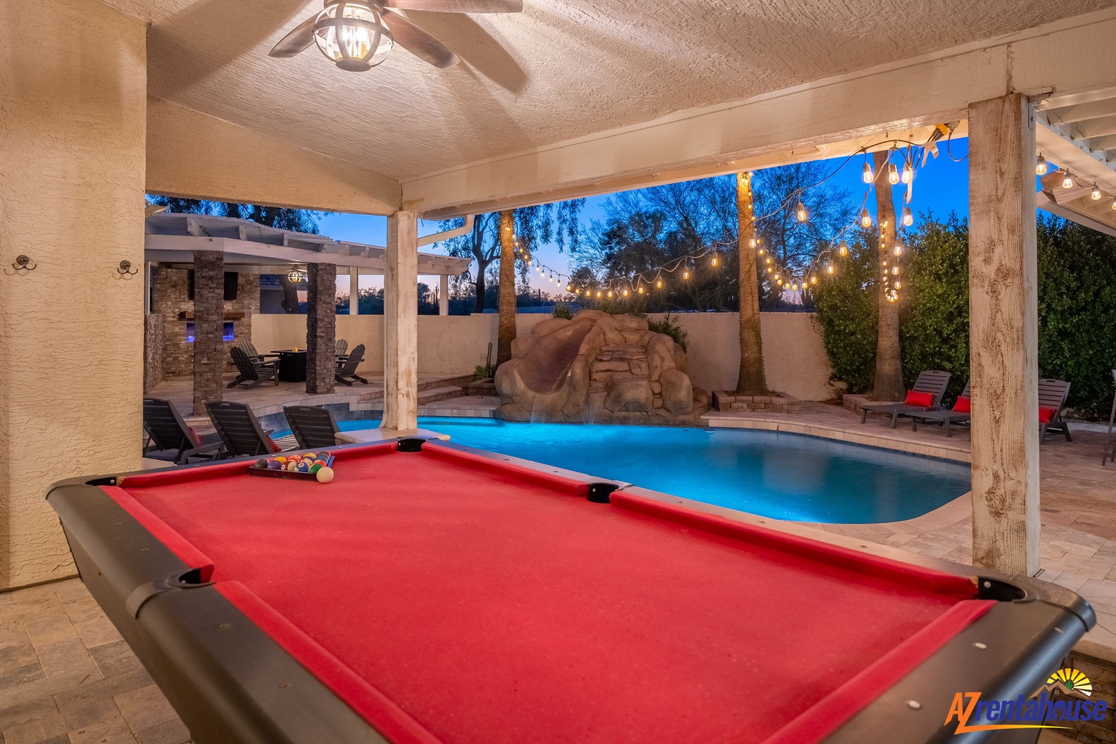 Enjoy evening games by your illuminated pool, with a grotto waterfall and string lights creating a magical backyard retreat as dusk settles in.