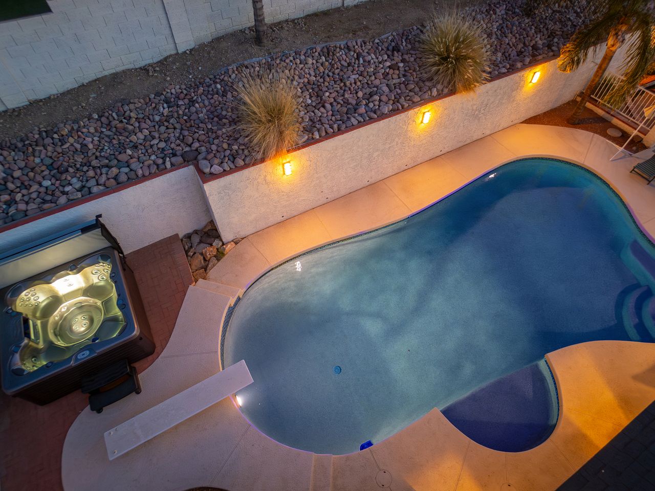 Aerial view of the private pool and hot tub area, illuminated with warm lighting and surrounded by desert landscaping with decorative rock and native plants.