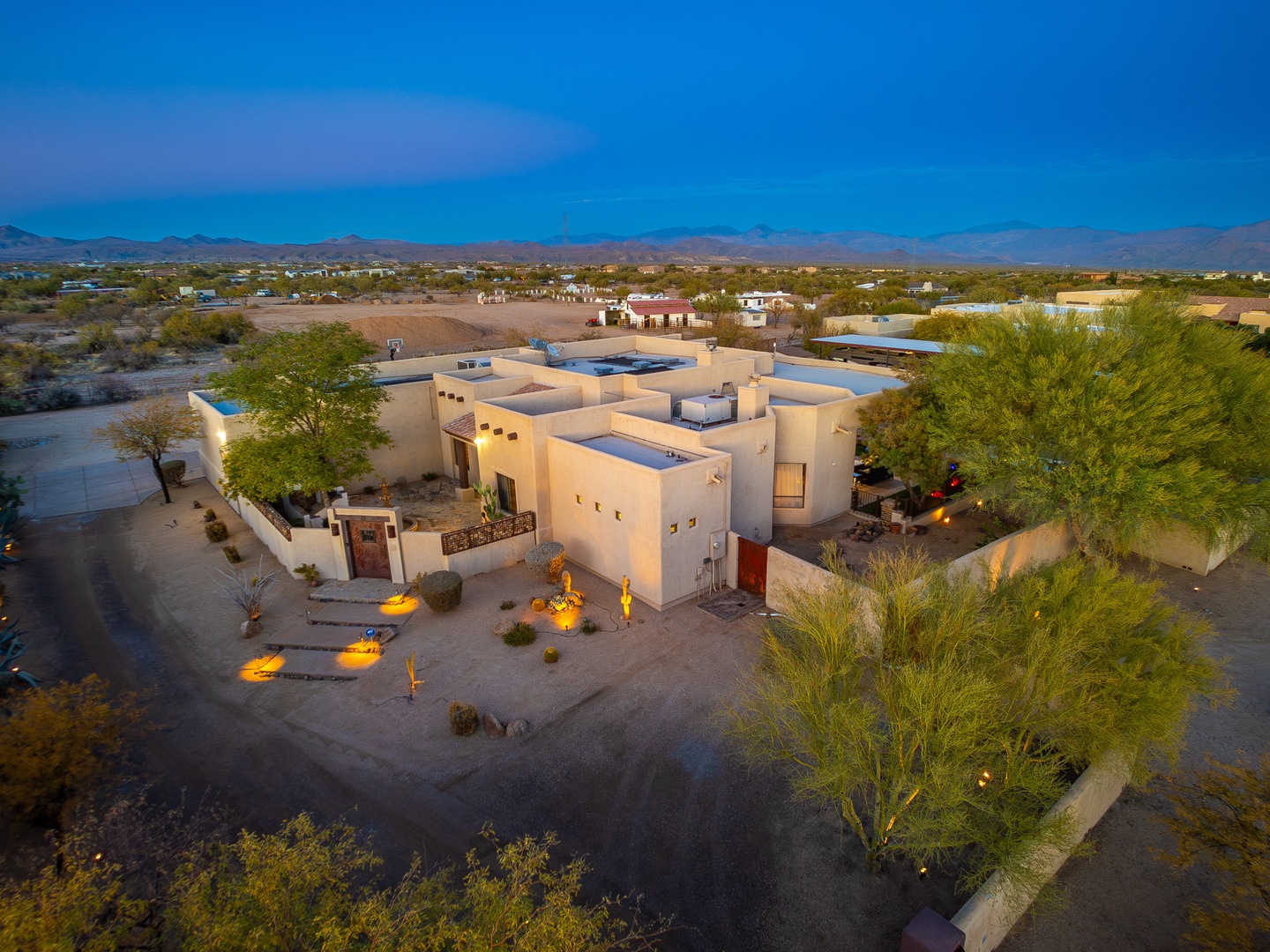 A stunning desert property with Southwestern architecture bathed in twilight glow, set against dramatic mountain views and expansive natural landscape, surrounded by lush native vegetation.
