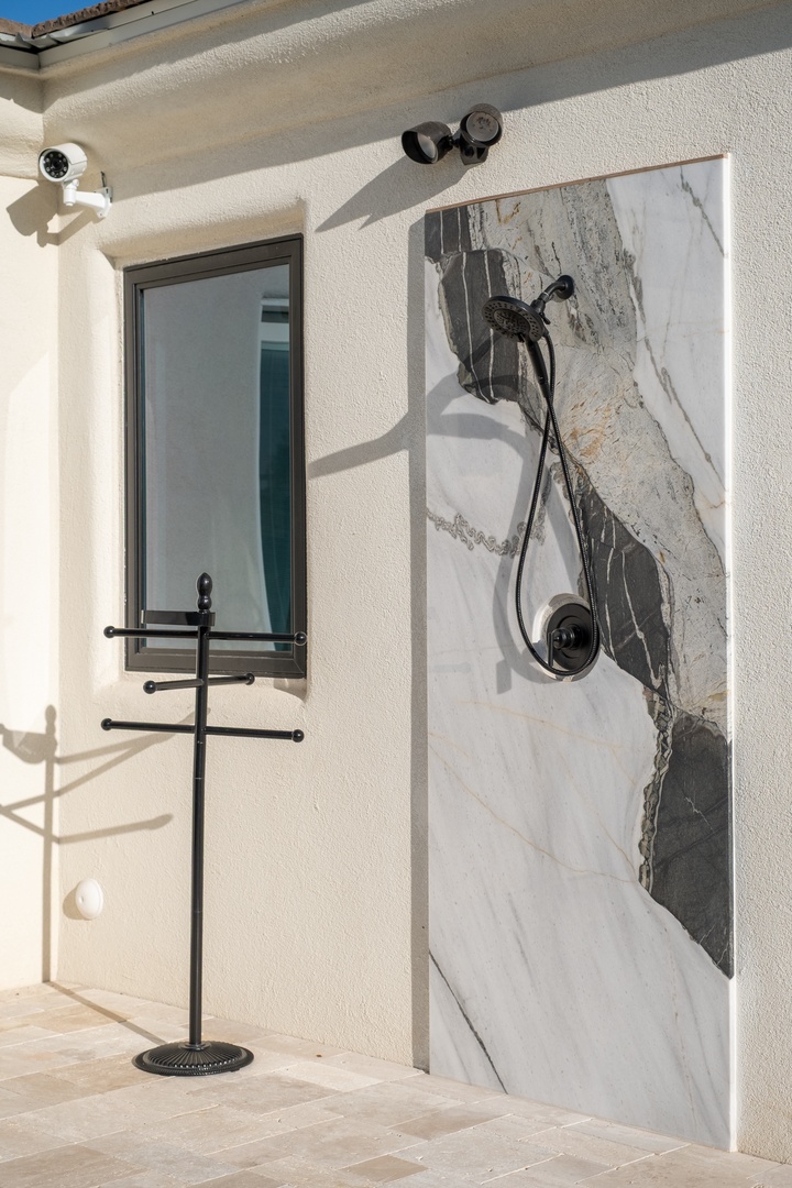 Modern outdoor shower with elegant marble-style wall and matte black fixtures creates a spa-like experience under the open sky.