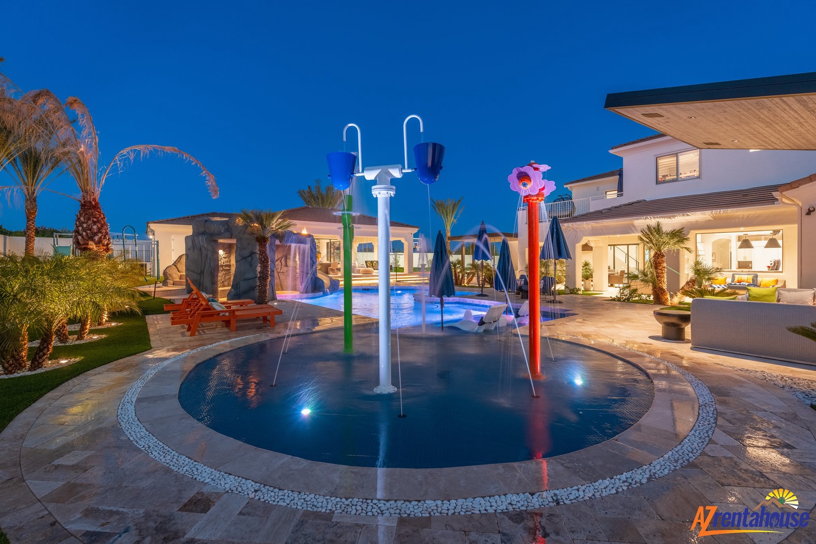 A stunning villa showcases its illuminated pool area with colorful water features against the deep blue evening sky.