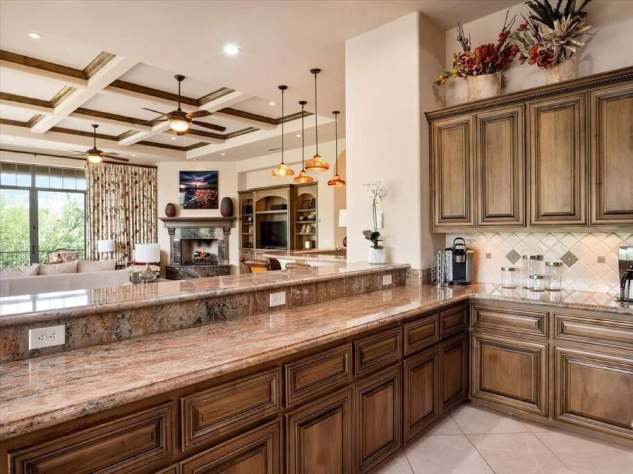 You'll love cooking in this spacious gourmet kitchen with stunning granite countertops, warm wood cabinetry, and elegant coffered ceilings that open to a cozy living area with fireplace and scenic views.