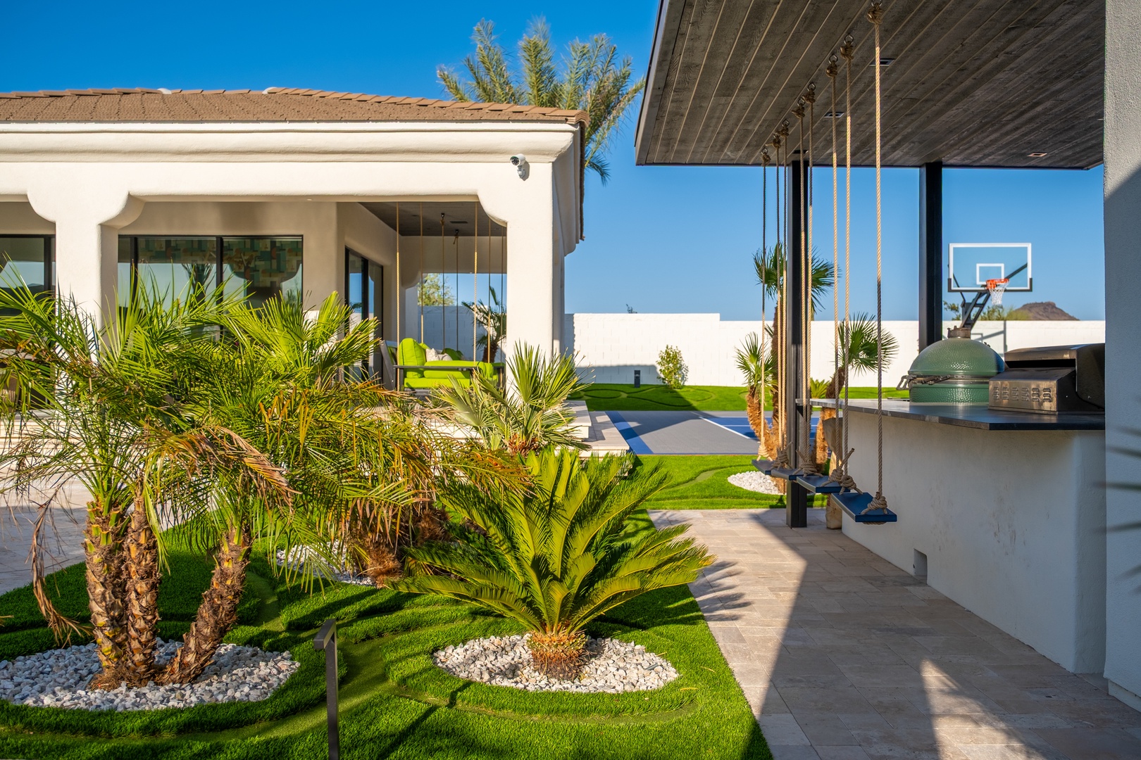 This modern desert retreat features landscaped grounds with palm trees, a private basketball court, and an outdoor kitchen with BBQ—perfect for active stays and entertaining under sunny skies.