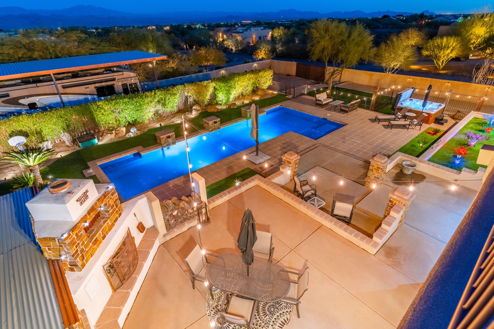 A beautifully lit evening backyard featuring dual pools, spa, outdoor lounging, and mountain views—your private desert oasis awaits under the stars.