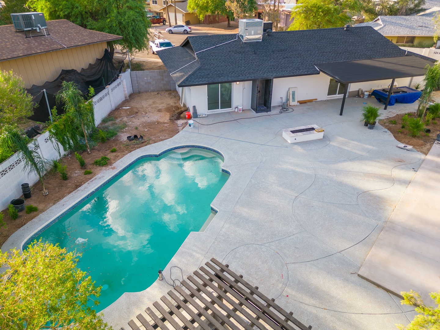 Aerial view of a residential vacation rental featuring a private swimming pool, spacious patio, and covered outdoor area in a quiet neighborhood setting surrounded by greenery.