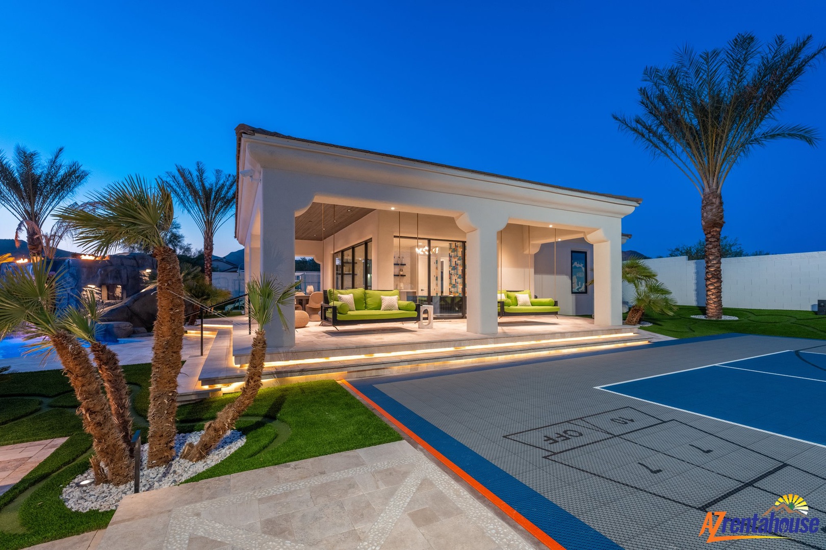 Modern luxury villa features illuminated pavilion, sports court, and tropical palms creating an upscale resort atmosphere.