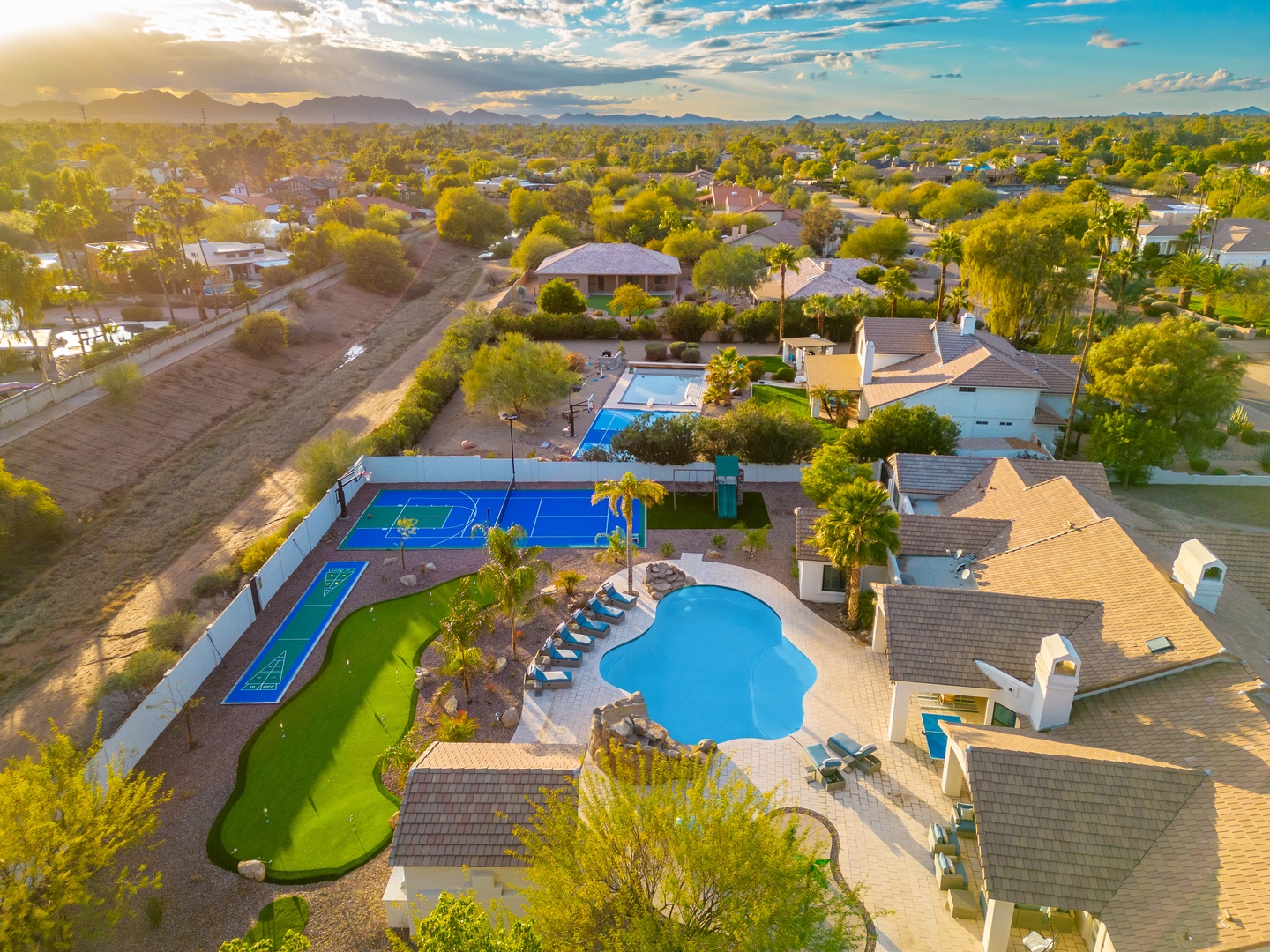 Aerial view captures the property's expansive vacation complex with resort-style amenities including multiple pools, a pickleball court, and putting green, all set against mountain views and neighboring residential areas.