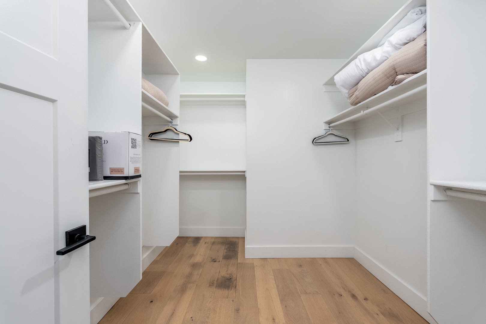 Step into your spacious walk-in closet, where crisp white shelving and warm wood floors keep your wardrobe organized and easily accessible throughout your stay.