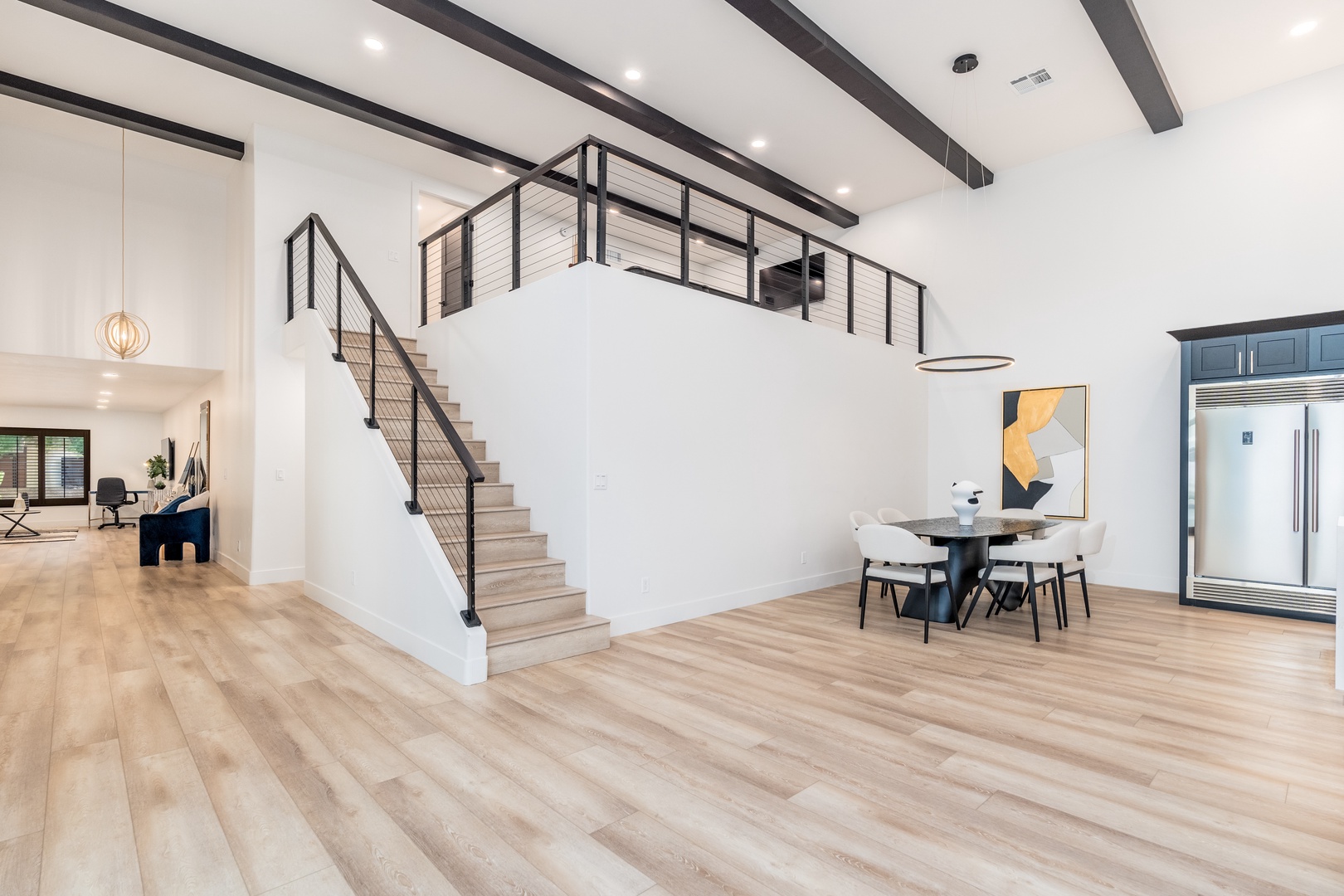 Soaring ceilings and dramatic beams frame your open-concept living space, where a striking loft overlooks the dining area. Sleek modern design meets warm wood tones throughout.