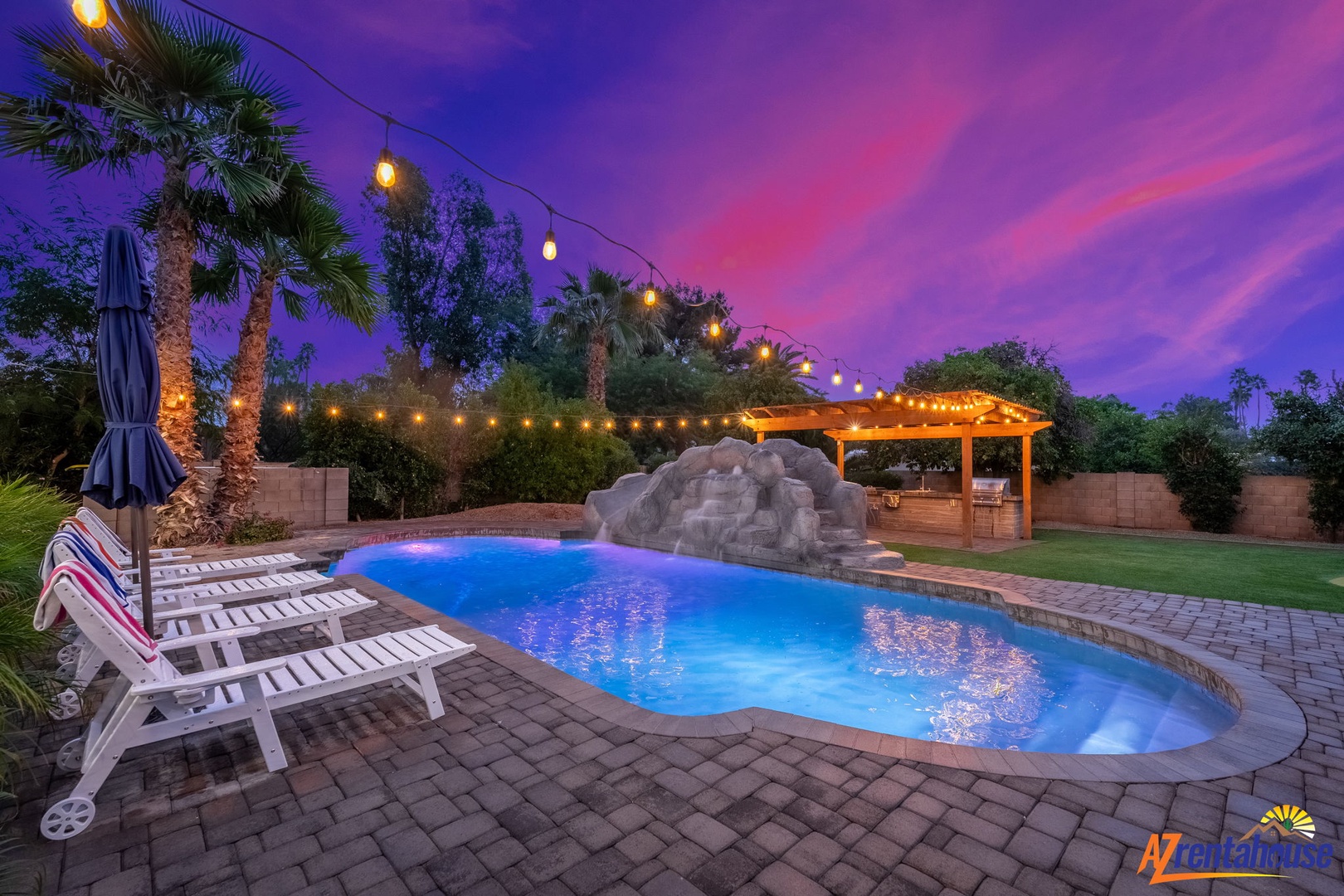 Stunning twilight pool area with dramatic purple sky, string lights, and waterfall feature creating your perfect desert oasis retreat.
