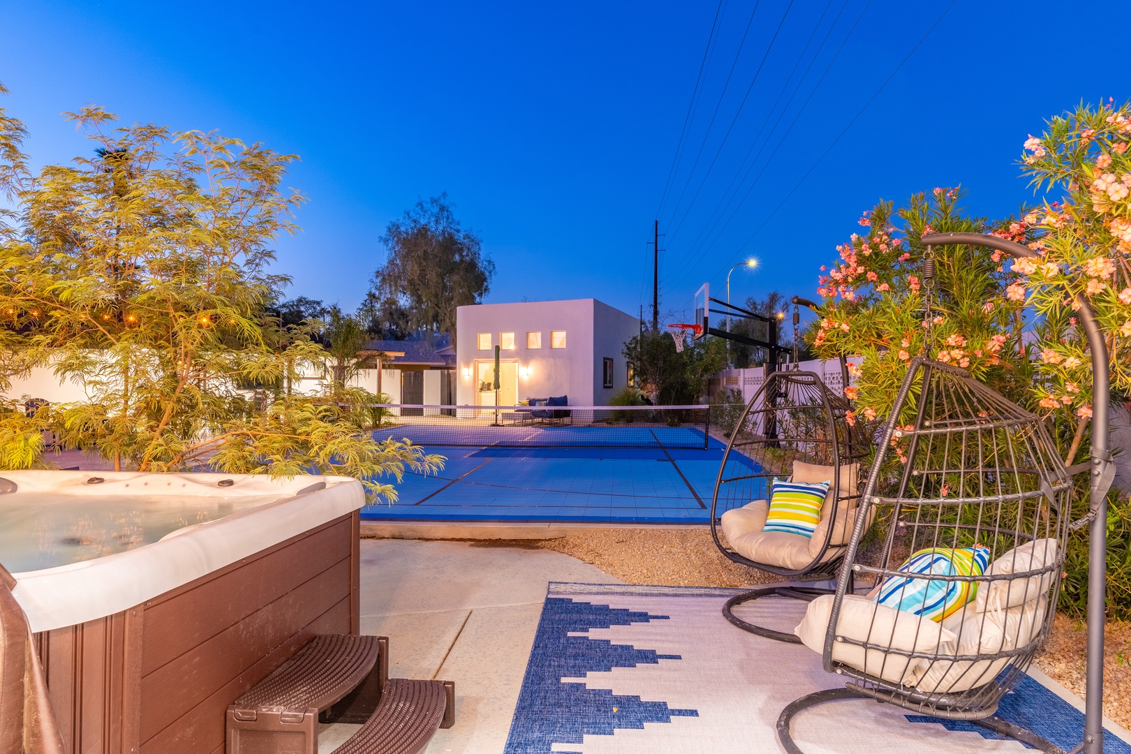 Modern pool area with hot tub and swing seats lit under evening skies, surrounded by greenery and contemporary architecture.