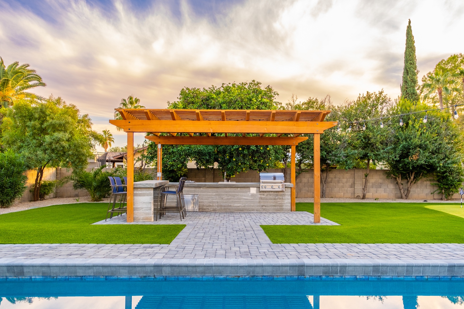 Gather under the pergola at your outdoor kitchen bar, perfectly positioned by the pool for effortless entertaining and sunset views.