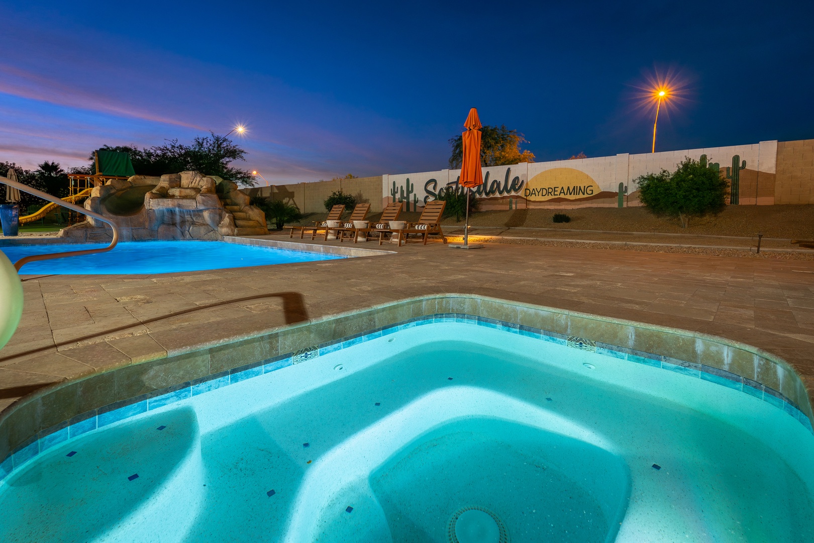 Evening descends on a Scottsdale resort featuring a hot tub, swimming pool with waterslide, and lounge chairs beneath desert sky—an inviting retreat after a day exploring the area.