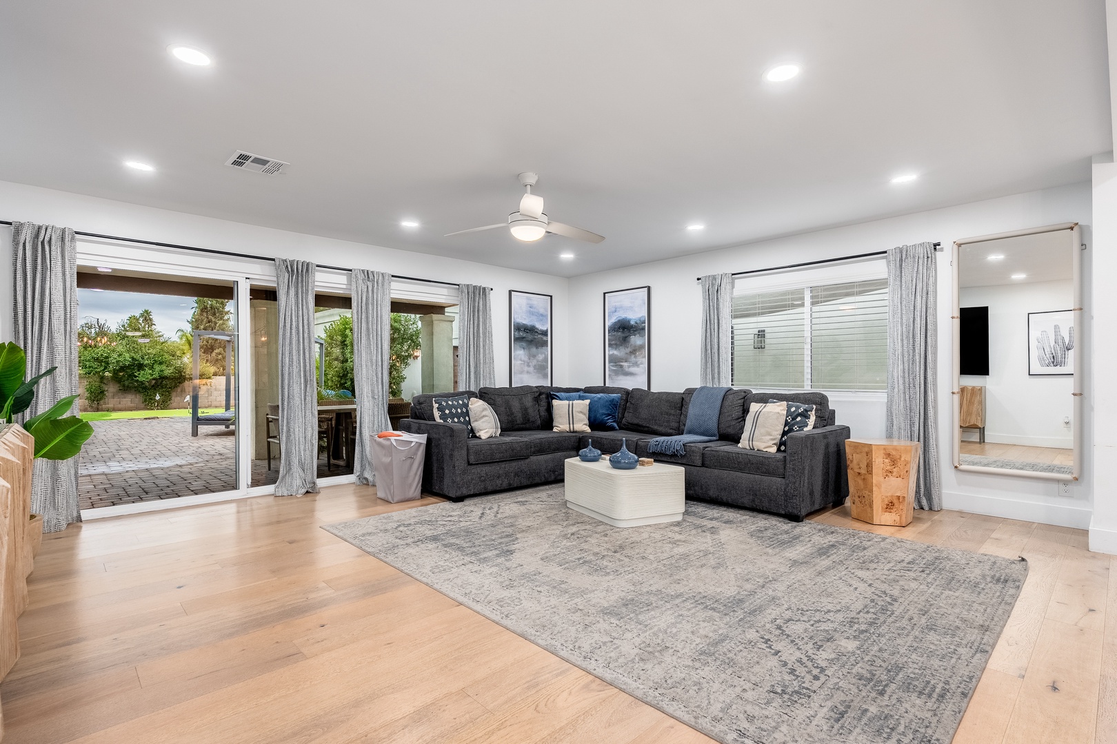 Unwind in your spacious living room featuring plush sectional seating, stylish décor, and floor-to-ceiling windows that flood the space with natural light and open to a private backyard oasis.