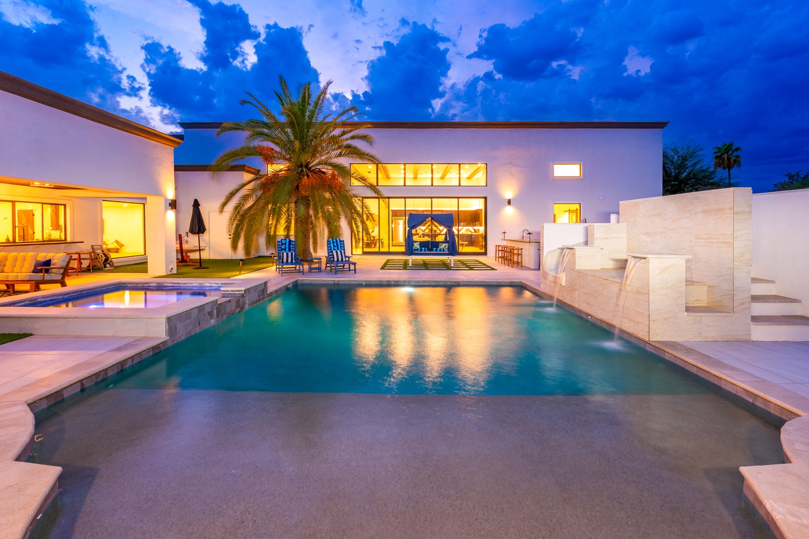 Modern vacation villa with private pool, contemporary architecture, and tropical landscaping—captured at dusk under a striking blue sky with illuminated interiors and outdoor seating areas.