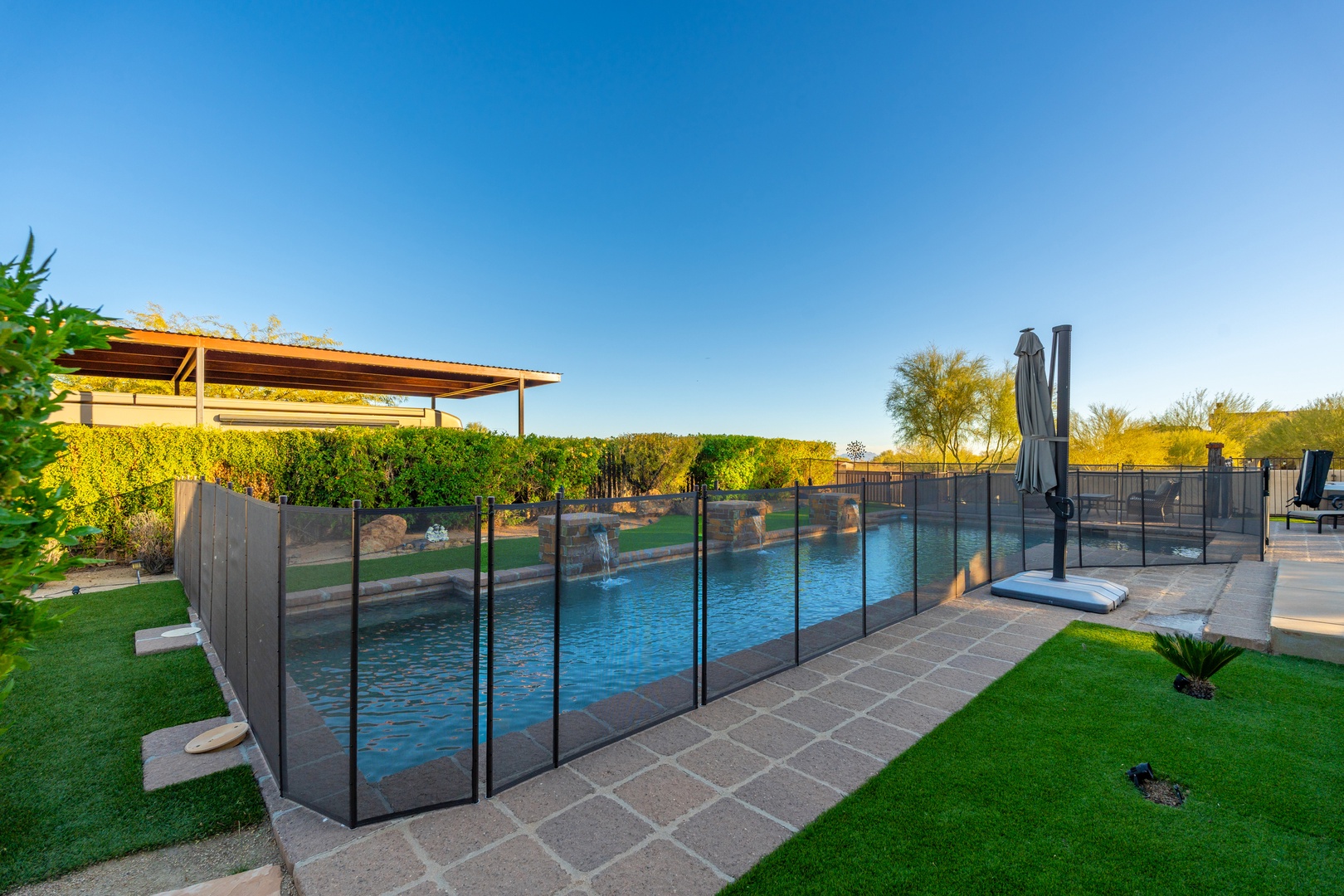 A sparkling pool awaits beneath clear desert skies, surrounded by lush green lawns and a shaded pergola—your private oasis for sun-soaked afternoons and refreshing dips.