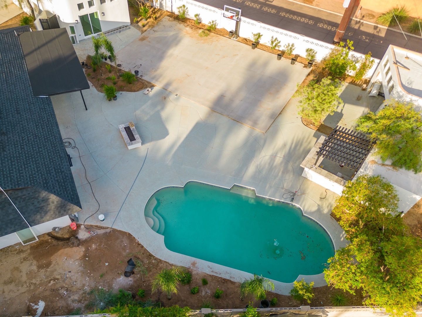 Aerial view showcasing the property's private pool, spacious outdoor recreation area with basketball court, pergola-covered seating, and lush landscaping in a quiet residential setting.