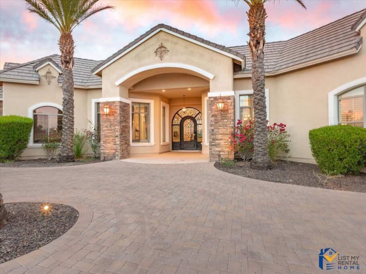 Elegant stone-accented entrance with manicured landscaping and towering palm trees welcomes arrivals to this luxury desert retreat.