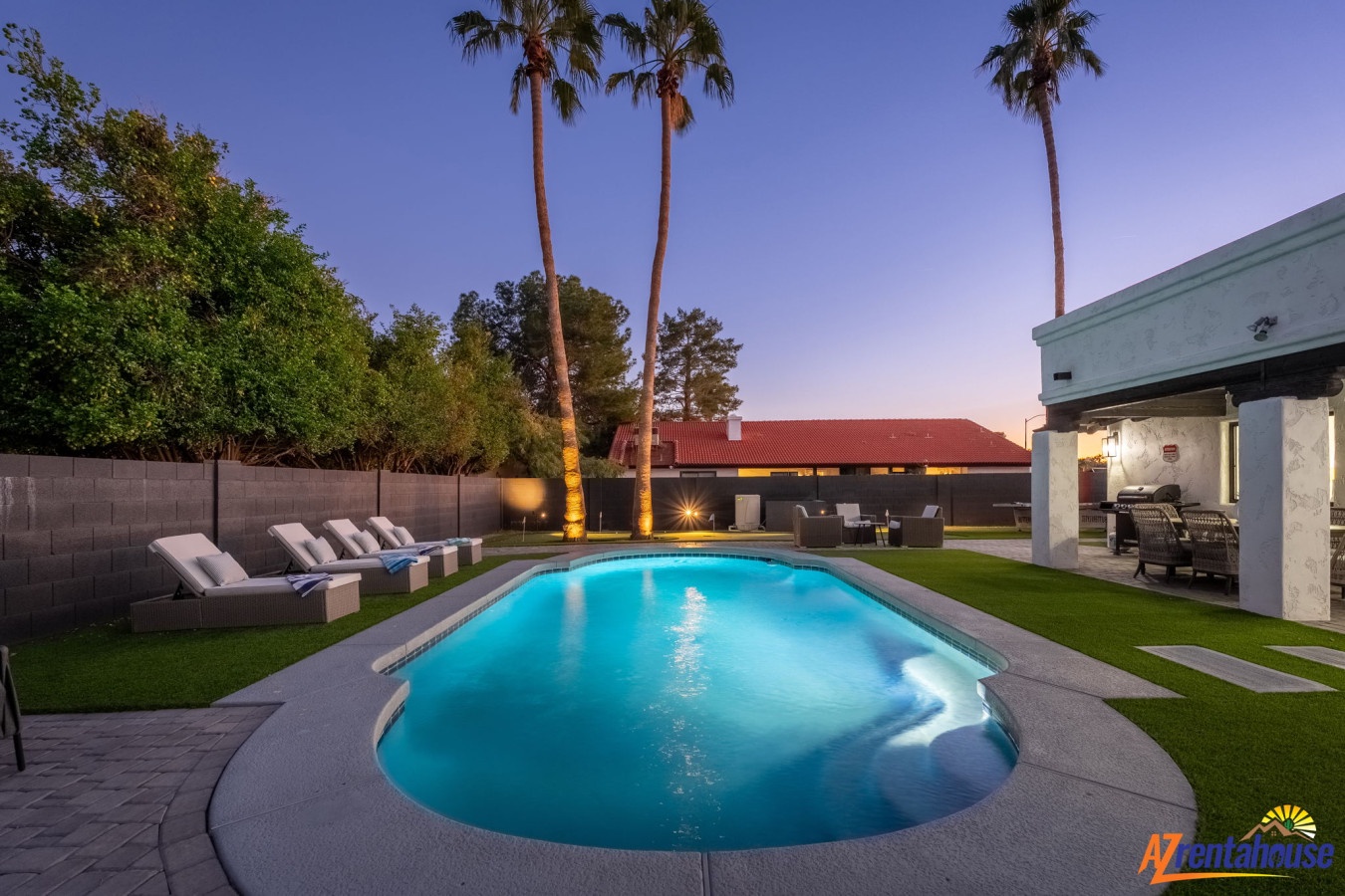 Modern backyard oasis with sparkling pool surrounded by palm trees and outdoor dining space at twilight.