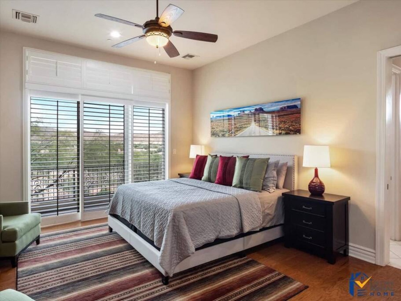 Unwind in your stylish bedroom featuring a plush queen bed, scenic artwork, and private balcony access with natural light streaming through elegant shutters.