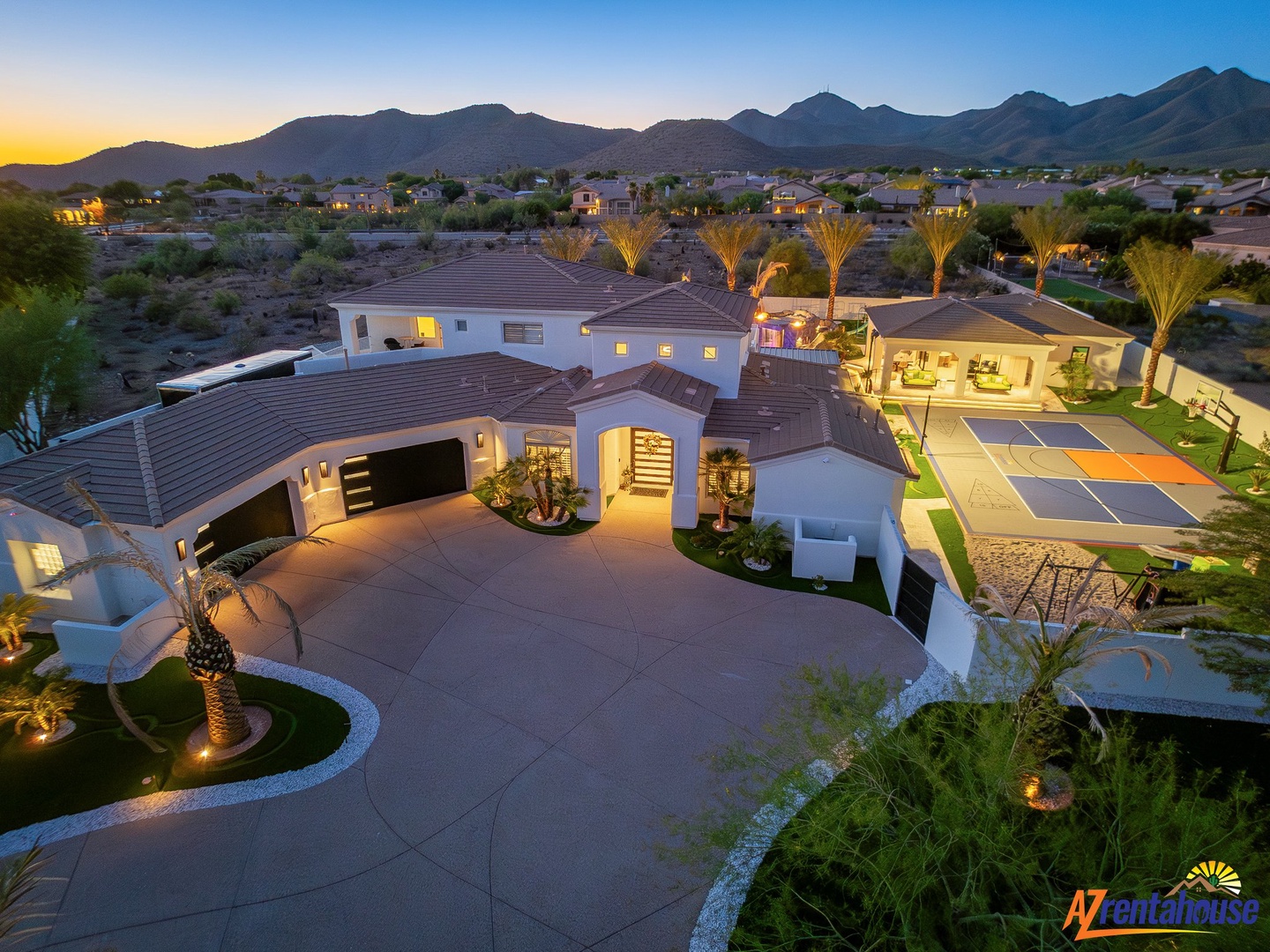 Luxurious desert estate with stunning mountain backdrop and illuminated sports court perfect for evening entertainment.