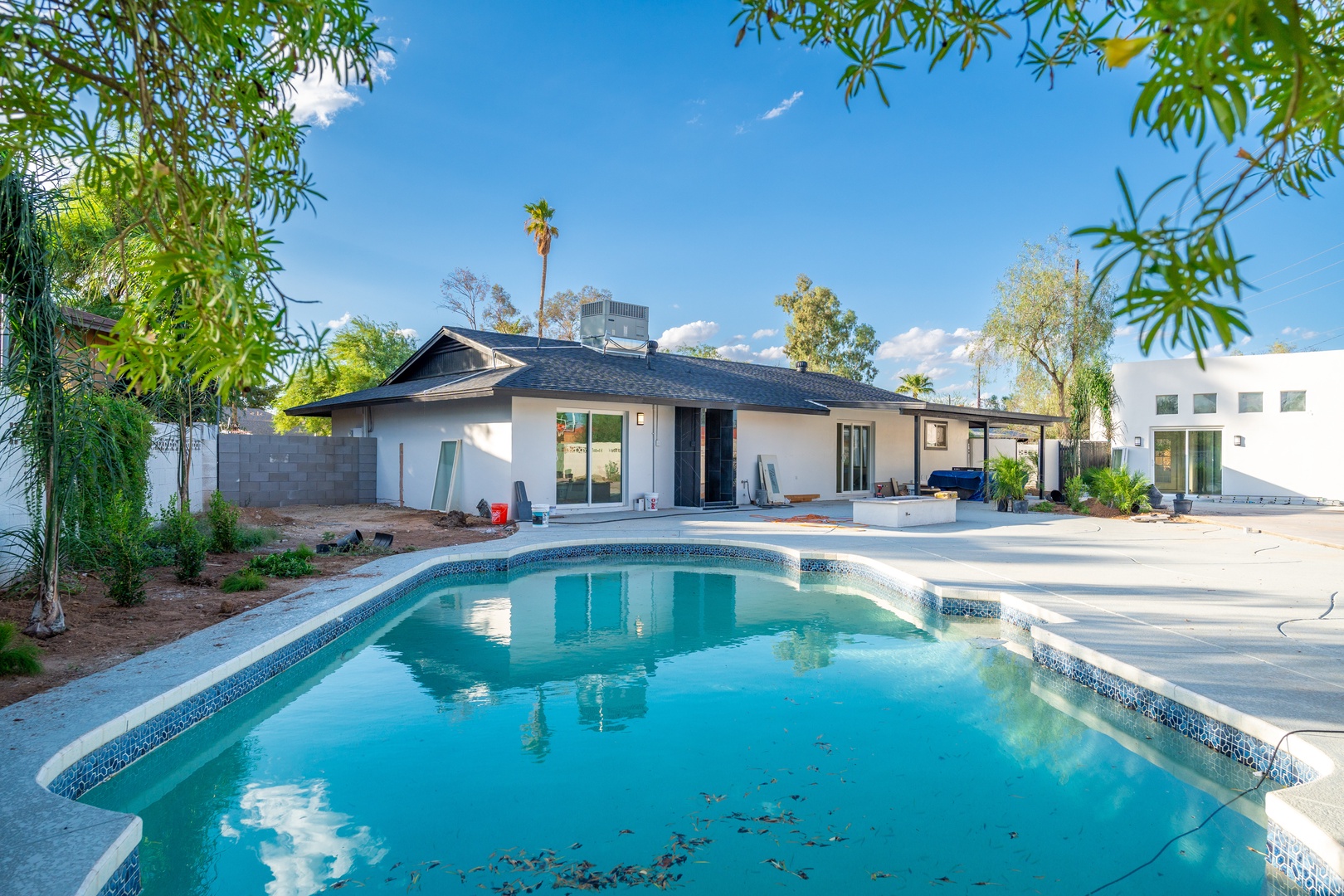 A sparkling pool framed by lush greenery and a spacious patio offers your perfect backdrop for sunny days and warm evenings under clear blue skies.