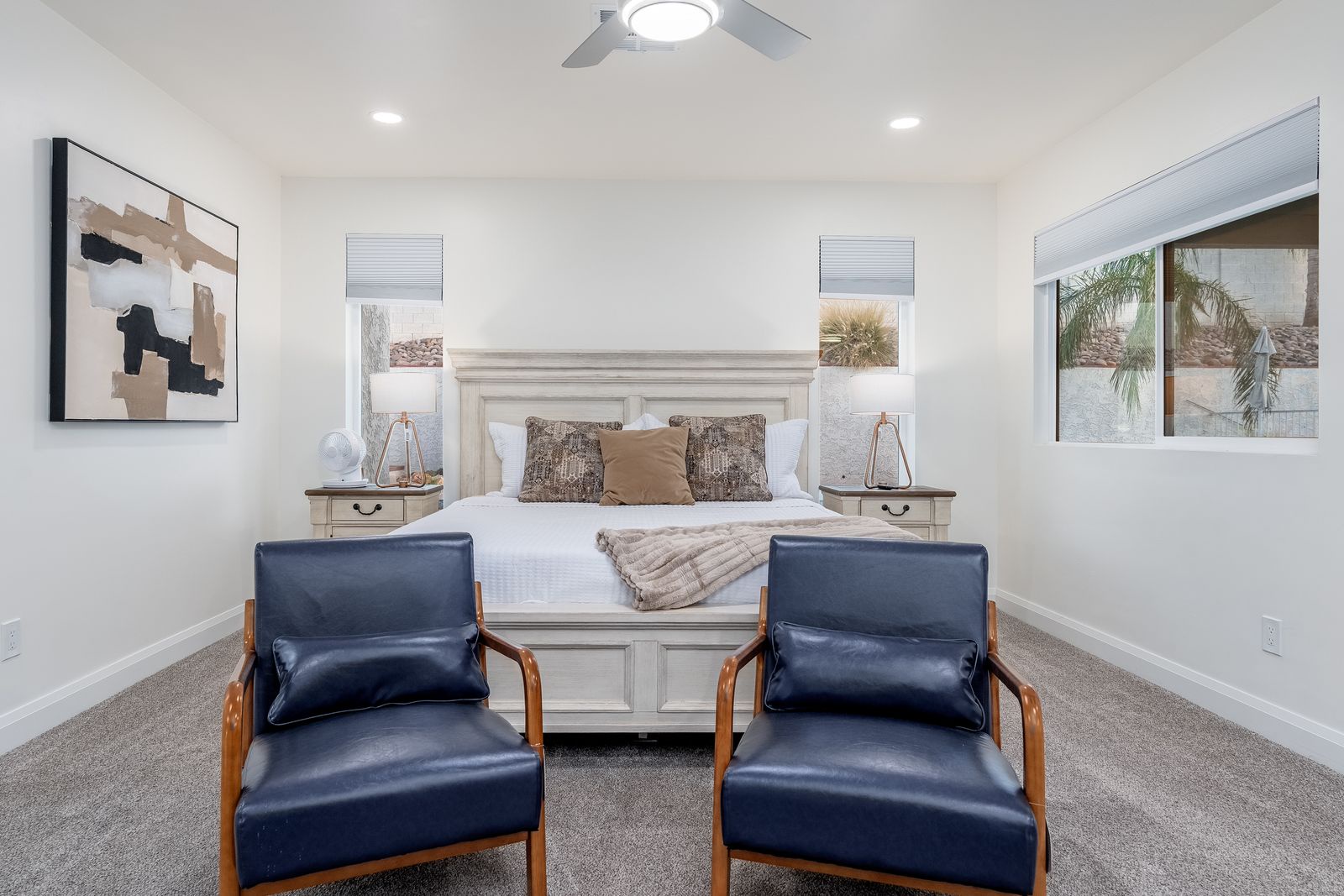 Sink into your cozy bed framed by soft natural light, with plush seating and coastal art creating your peaceful retreat. The ceiling fan keeps you comfortable year-round in this serene escape.