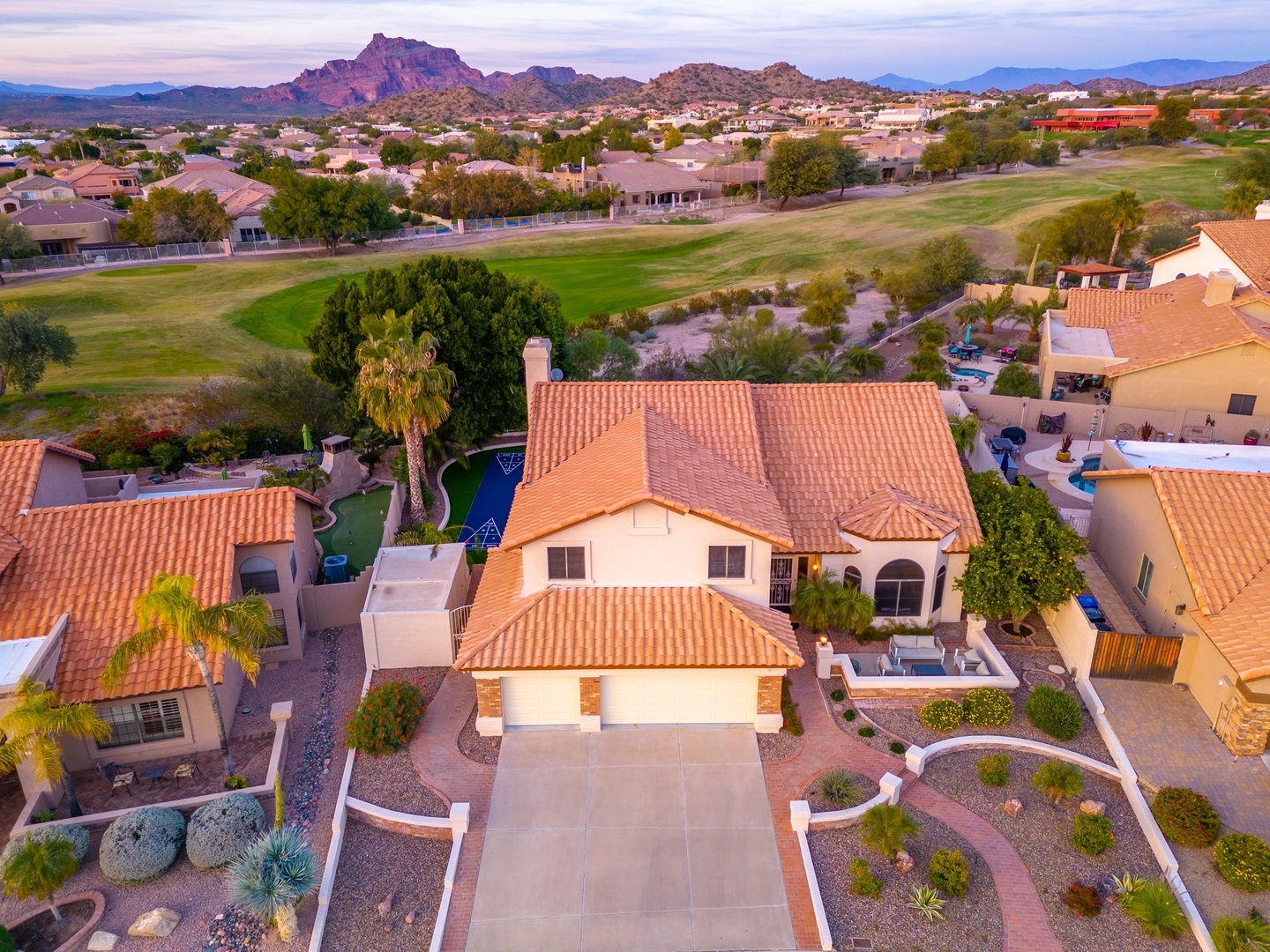 Aerial view showcasing the property's desert setting with golf course frontage and dramatic mountain backdrop at sunset.