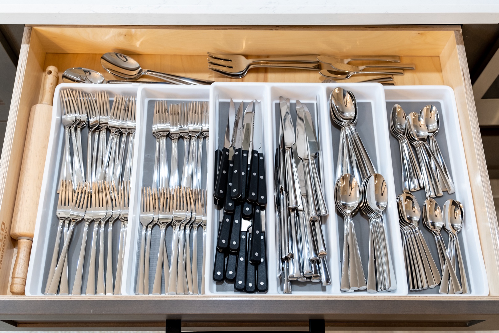 Open the drawer to find everything you need for dining—silverware, serving utensils, and kitchen tools neatly organized with a rolling pin ready for your culinary adventures.